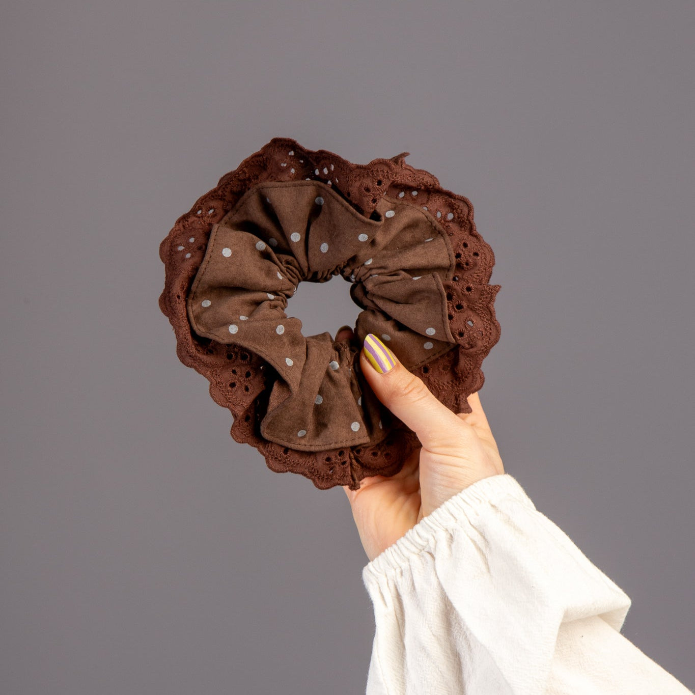 Hand houdt scrunchie met donkerbruin kant vast in studio
