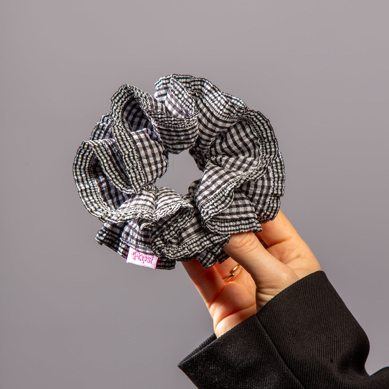 Hand houdt scrunchie met zwart-witte ruitjes vast in studio