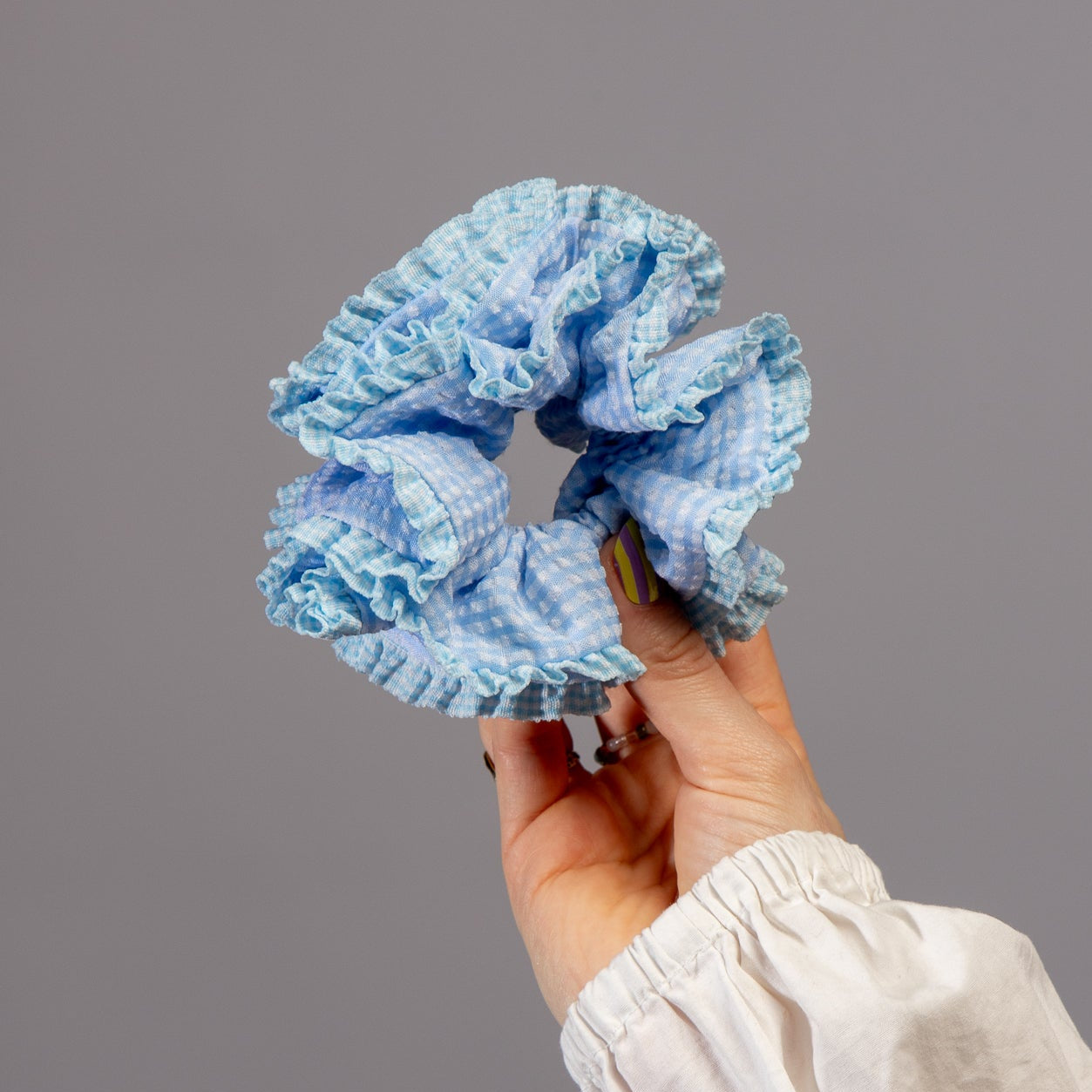 Hand houdt lichtblauwe scrunchie met ruitjes vast in studio