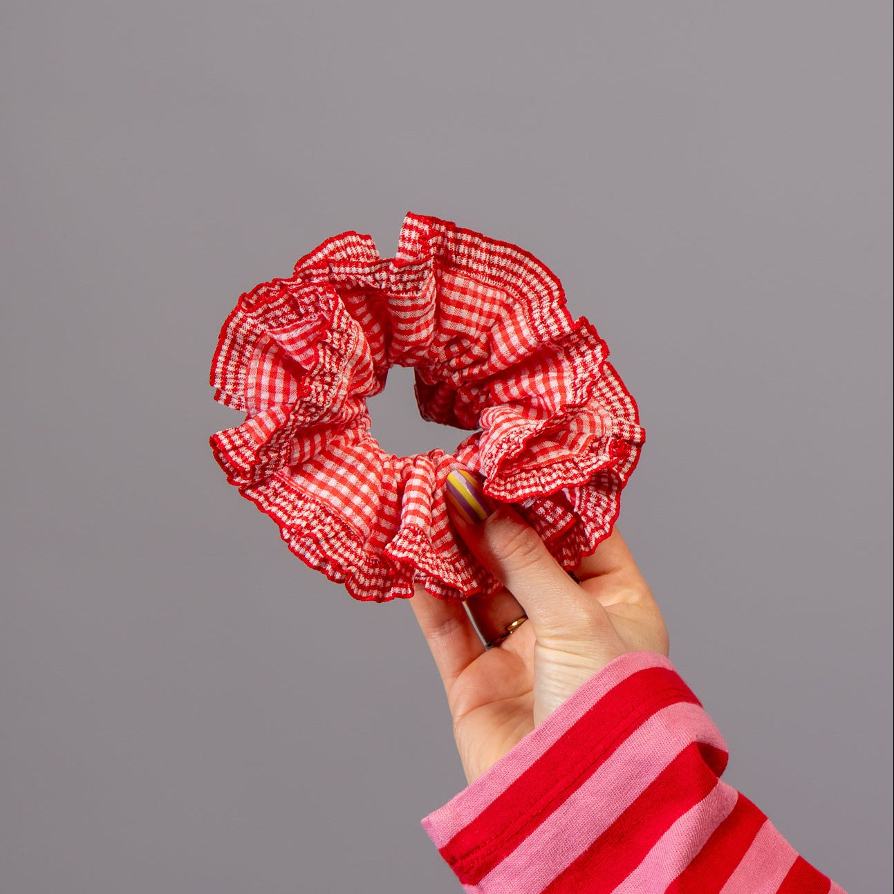 Hand houdt scrunchie met rode ruitjes vast in studio