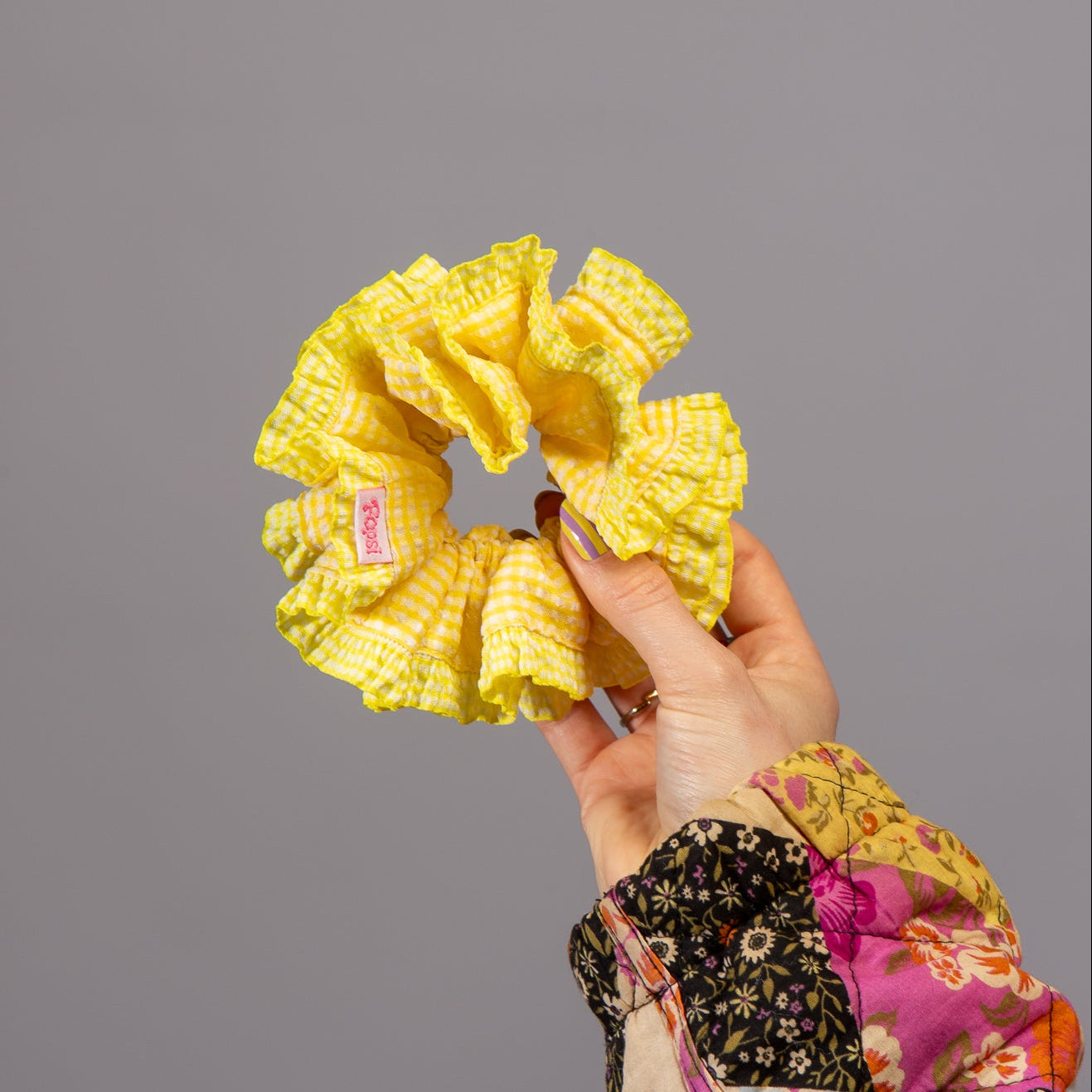 Hand houdt scrunchie met gele ruitjes vast in studio