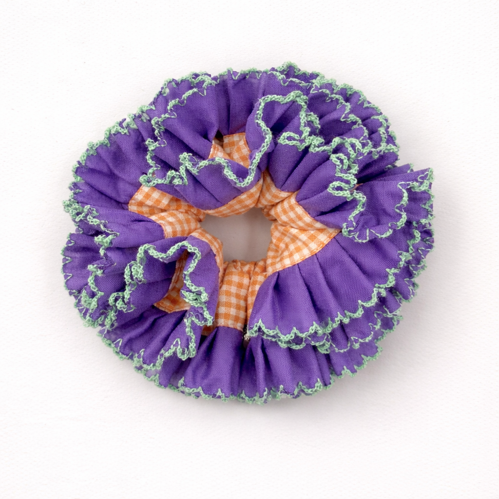 Productfoto van een paarse scrunchie met oranje ruitjes op een witte achtergrond