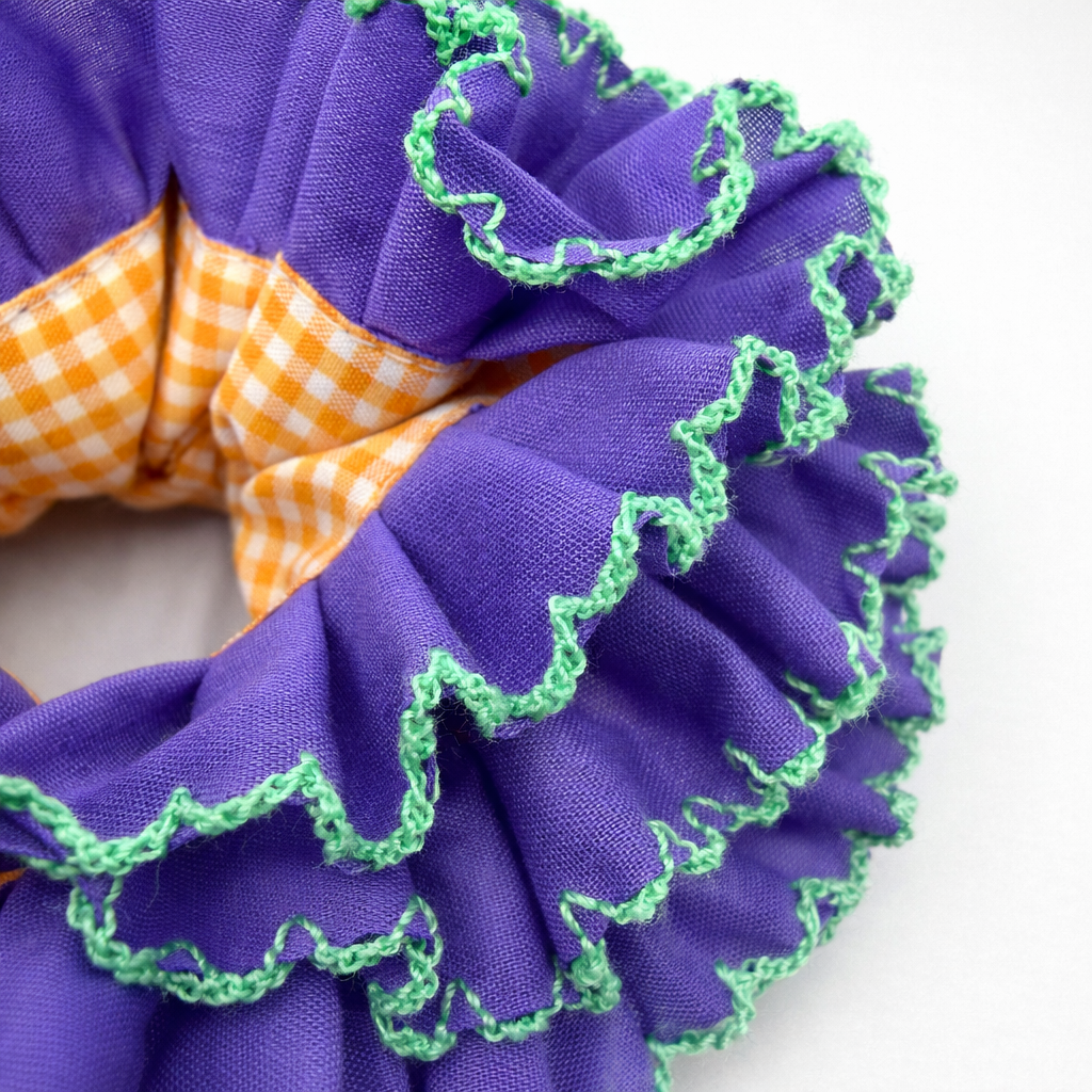 Detailfoto van paarse scrunchie met oranje ruitjes op witte achtergrond