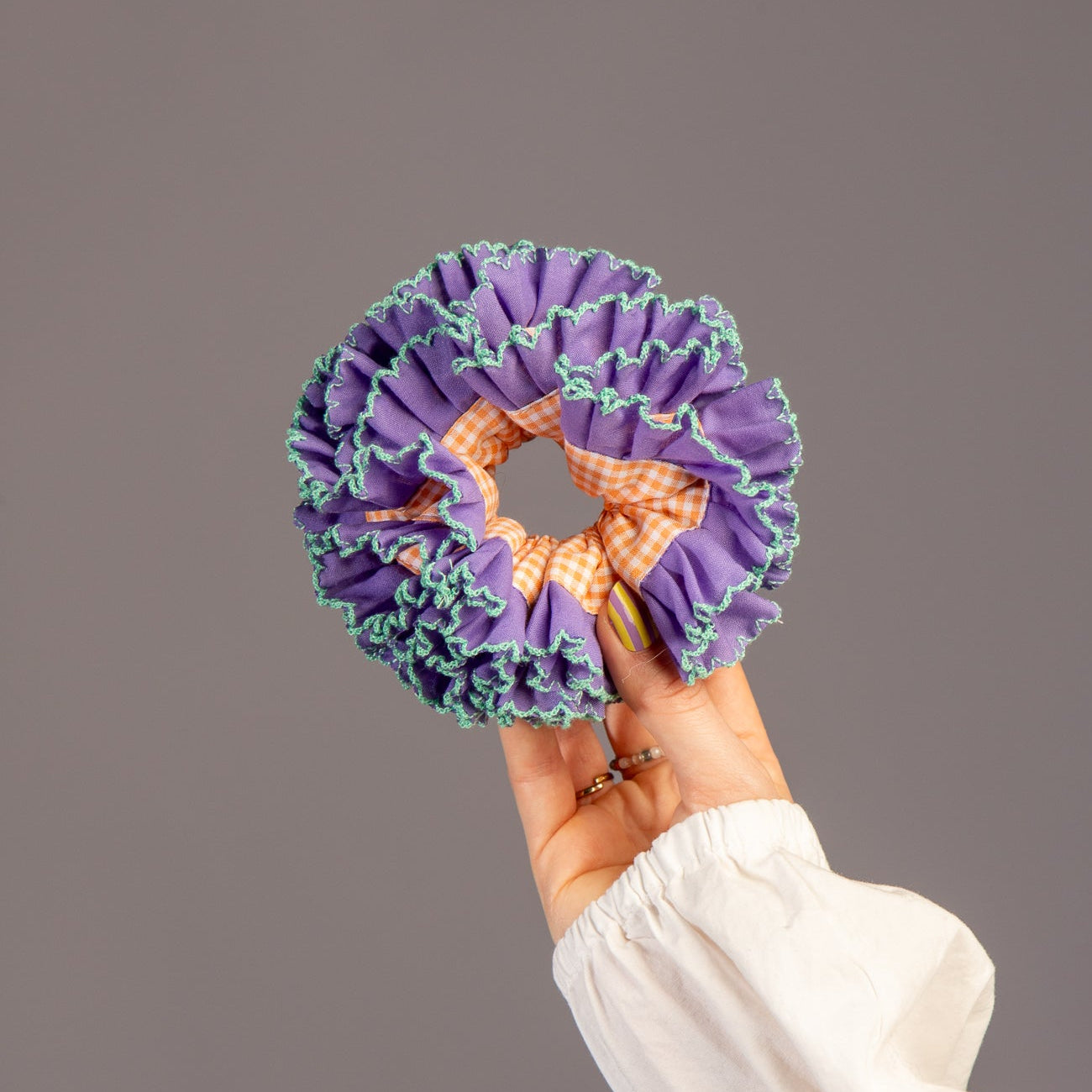 Hand houdt scrunchie met paars en oranje vast in hand in studio