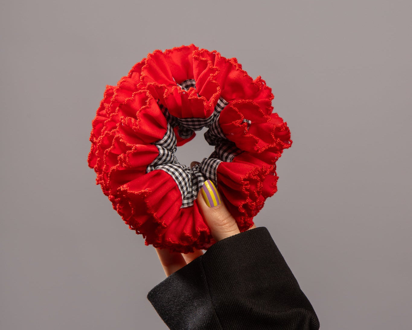 Foto van hand die rode scrunchie vasthoudt met zwart witte ruitjes