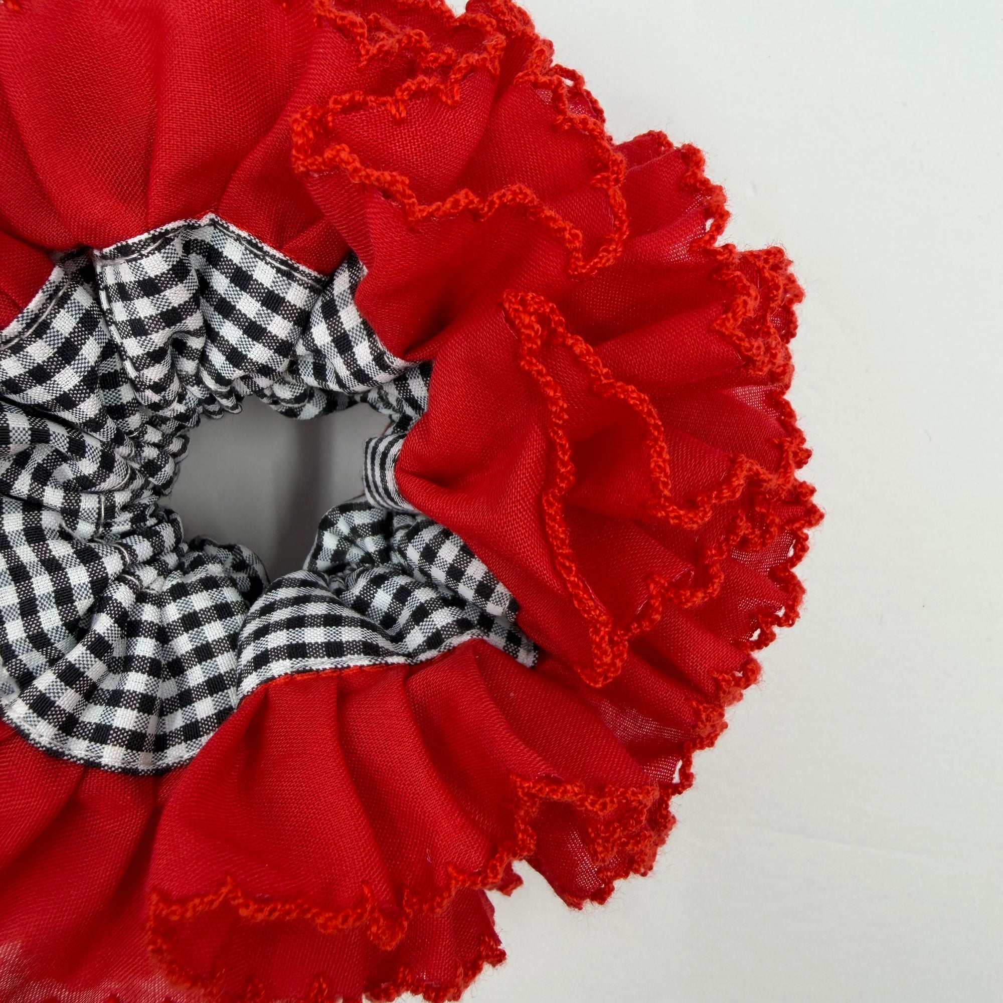 Detailfoto van een rode scrunchie met zwart witte blokjes op witte achtergrond