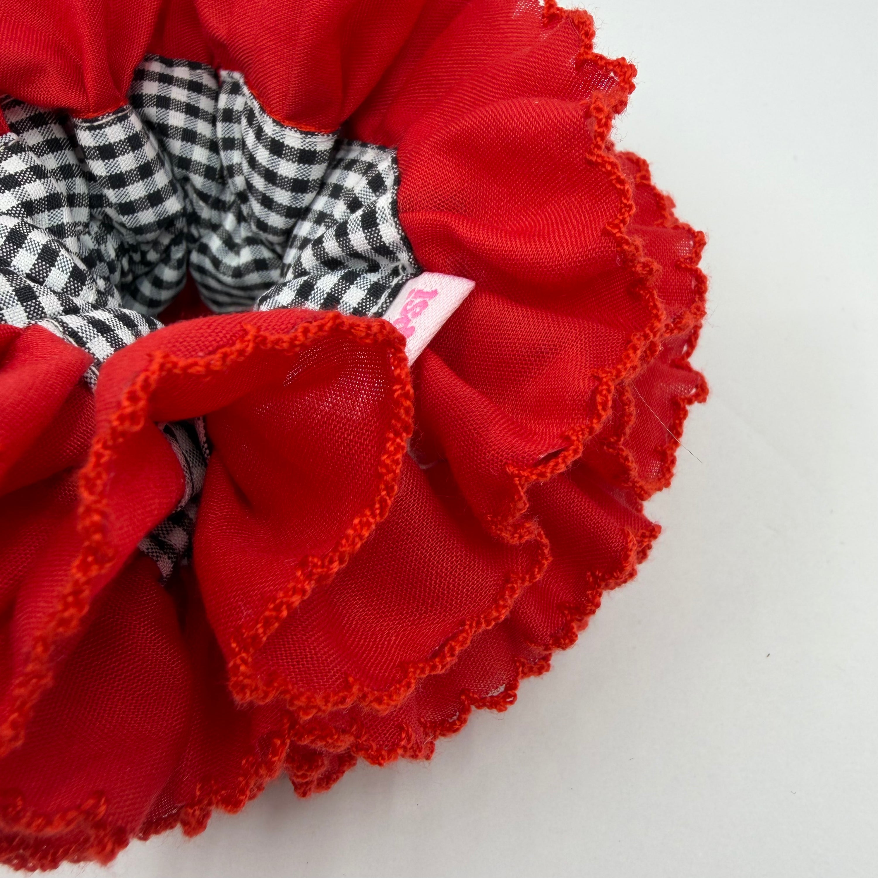 Detailfoto van een rode scrunchie met zwart witte blokjes op witte achtergrond