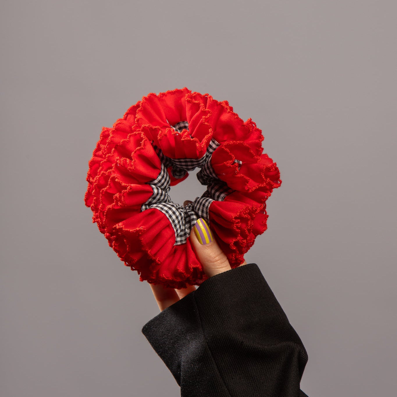 Foto van hand die rode scrunchie vasthoudt met zwart witte ruitjes