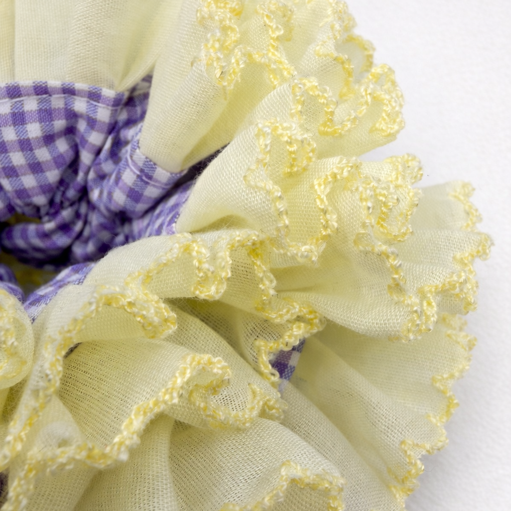 Detailfoto van een gele scrunchie met paarse ruitjes op witte achtergrond