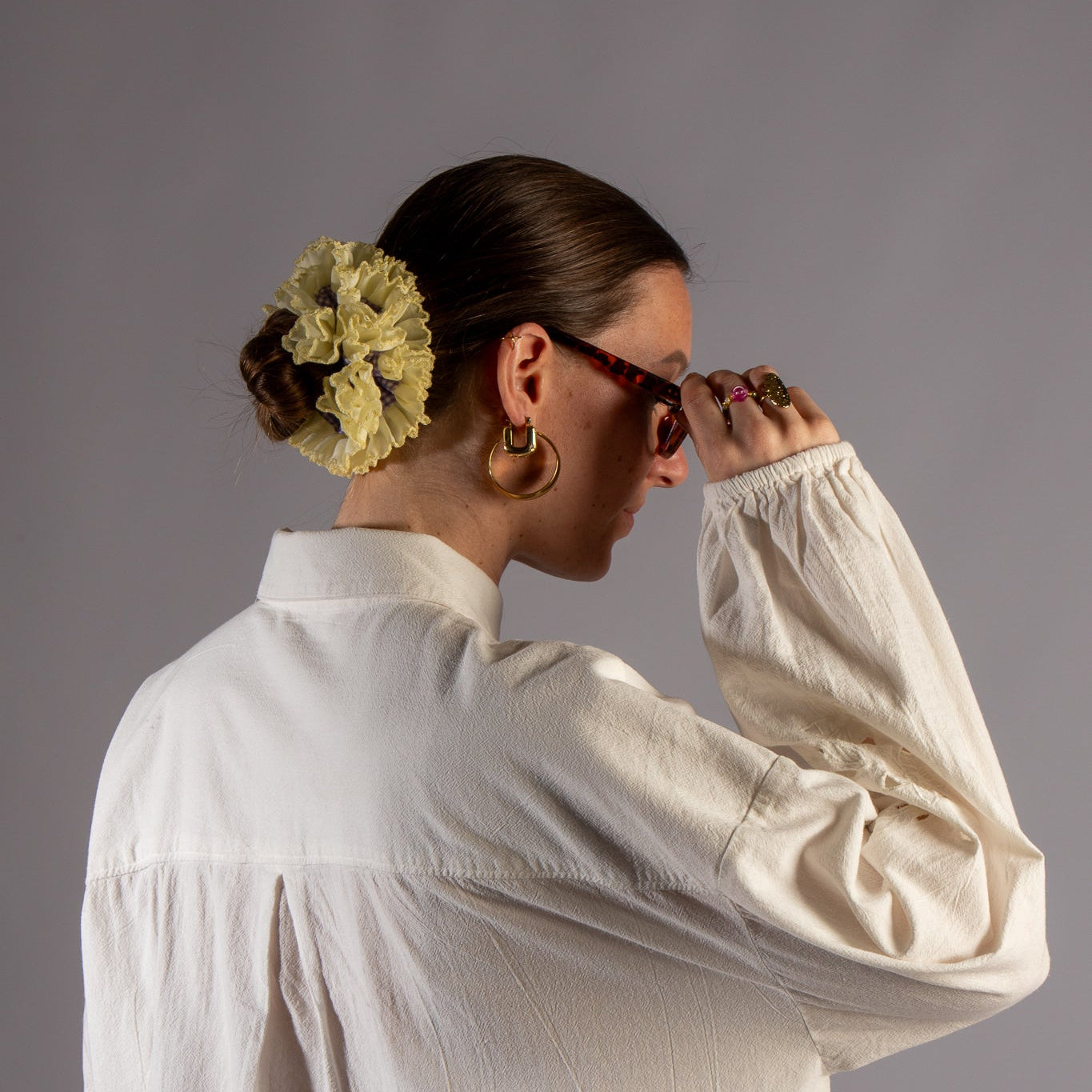 Model foto van zijkant met scrunchie in haar met witte blouse en bril