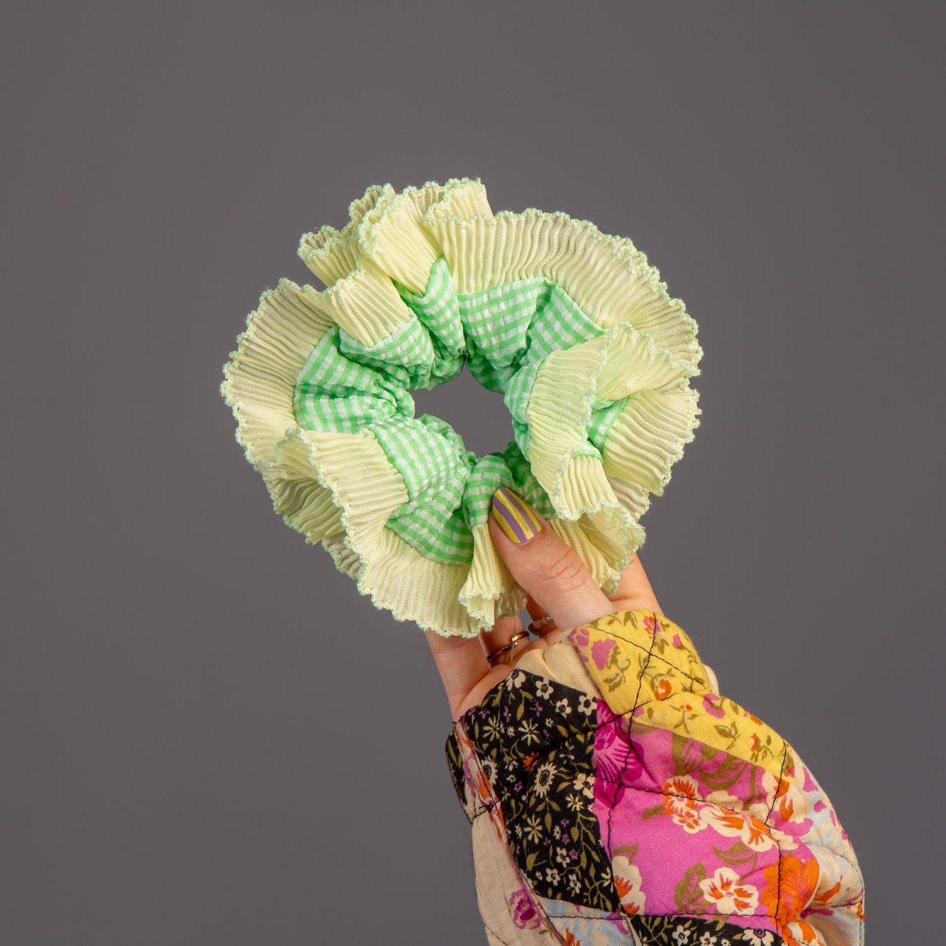 Hand houdt scrunchie met geel en groen vast in hand in studio