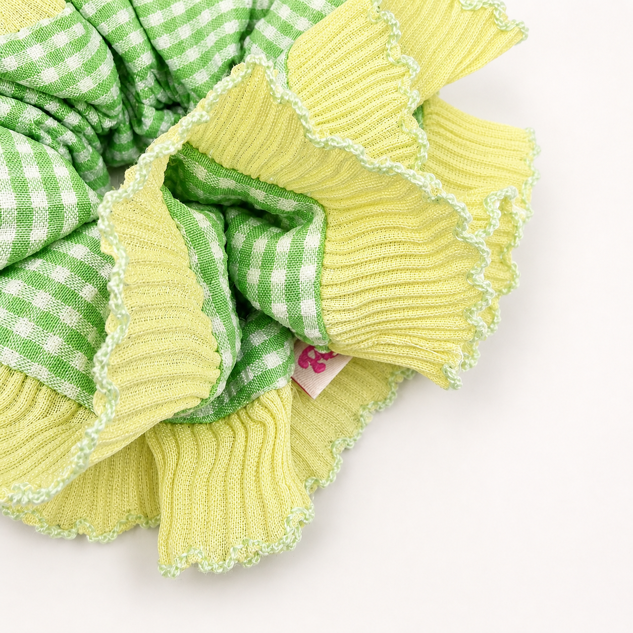 Detail foto van een geel met groene scrunchie met ruitjes op een witte achtergrond