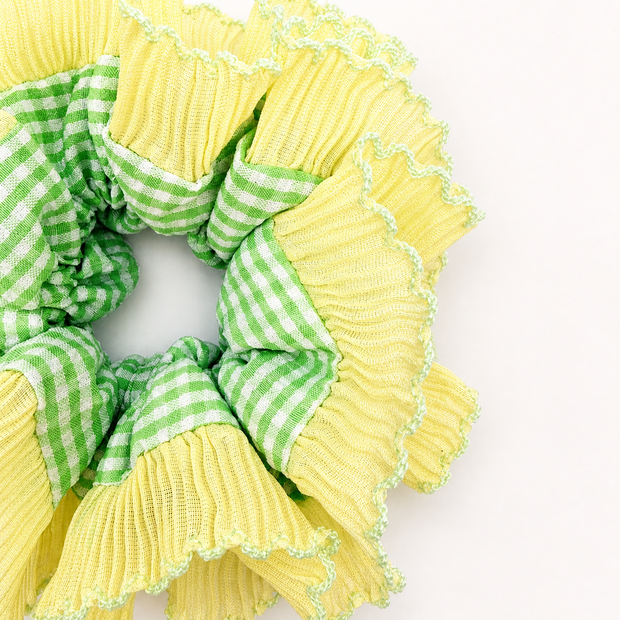 Detail foto van een geel met groene scrunchie met ruitjes op een witte achtergrond