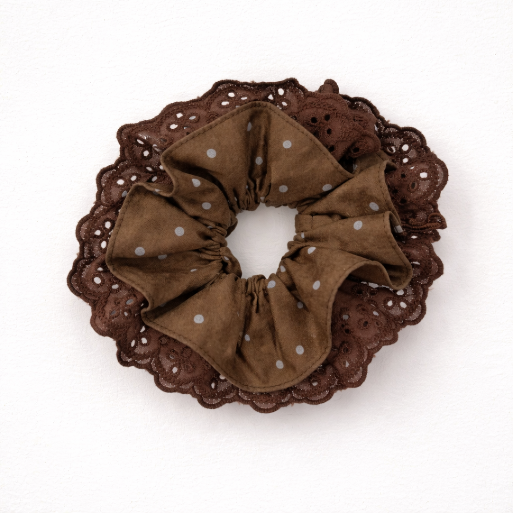 Productfoto van een bruine scrunchie met stipjes en velvet stof op een witte achtergrond